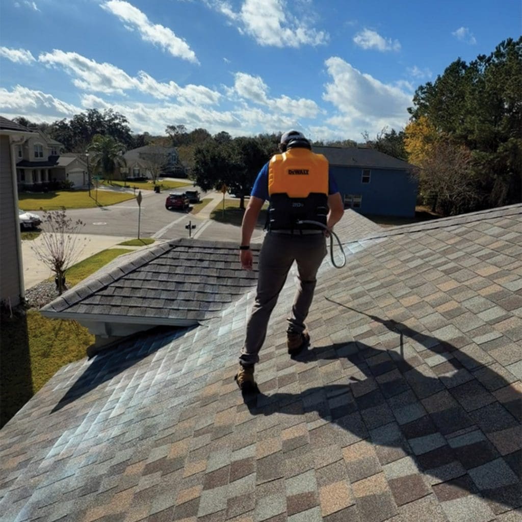 Florida roof rejuvenation technician with DeWalt backpack sprayer walking asphalt shingle roof in residential neighborhood
