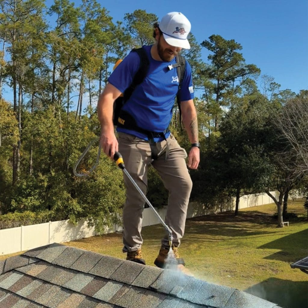 Florida roof technician spraying Shingle RX clear asphalt roof sealer along shingle edge with backpack sprayer